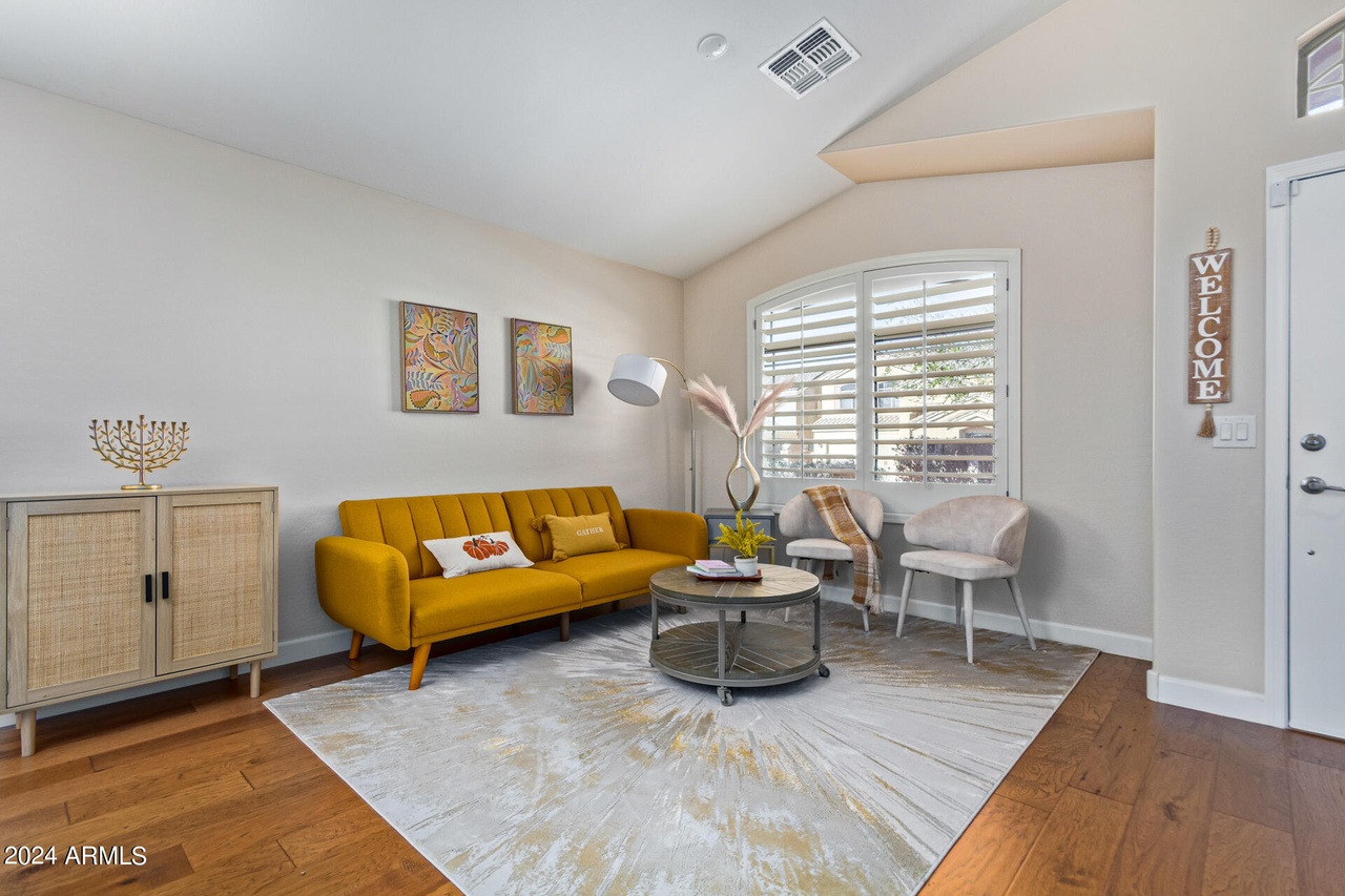 Staged living room with a mustard sofa, layered rug, and plantation shutters in a North Phoenix home